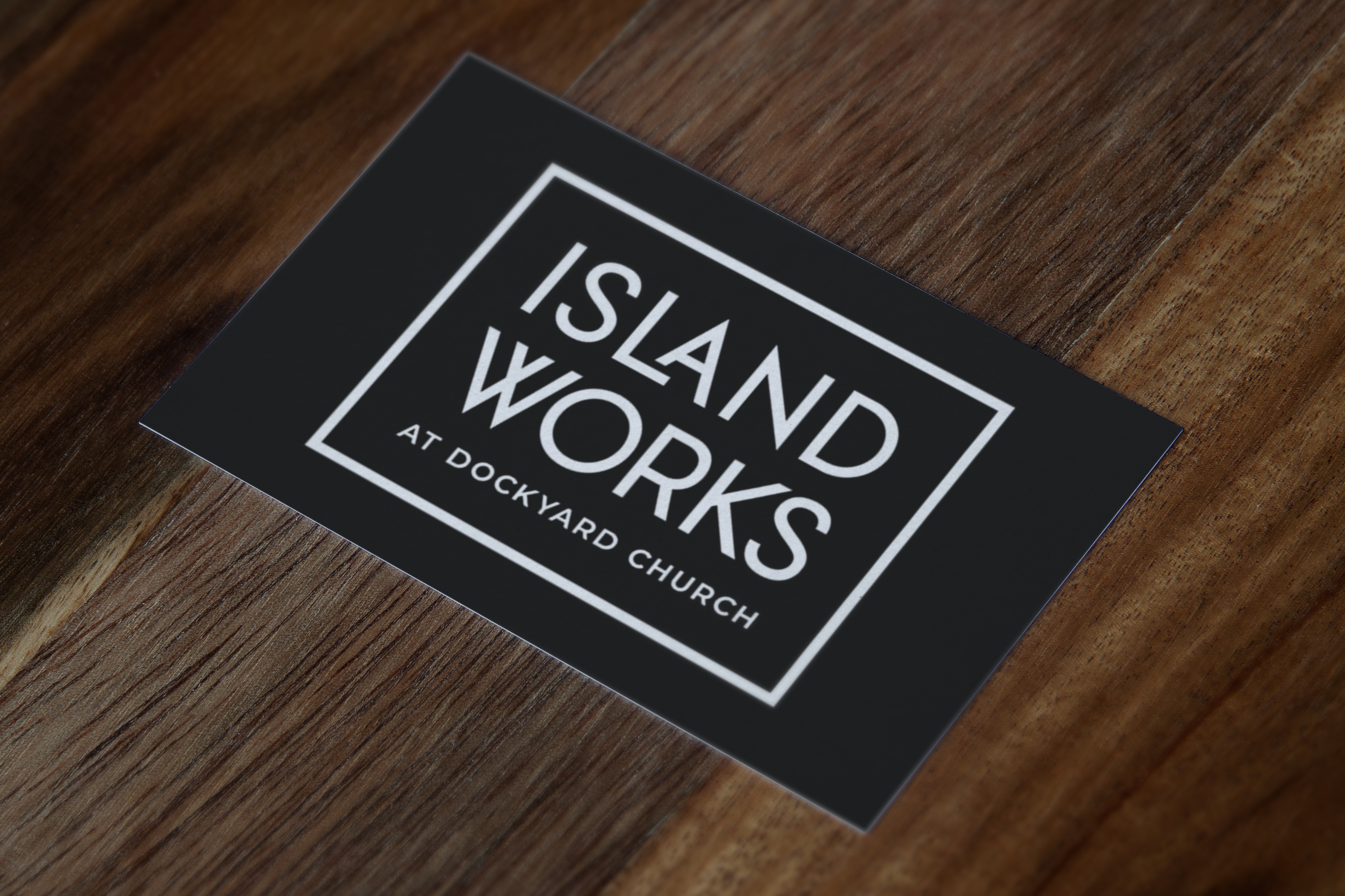 A photo of a gift card with the Islandworks logo on a blackbackground laying on a wooden table.